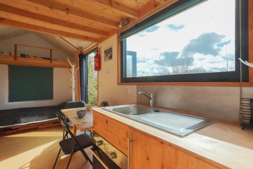 eine Küche mit einem Waschbecken und einem großen Fenster in der Unterkunft Très Jolie Tiny House Tout Confort in Prat