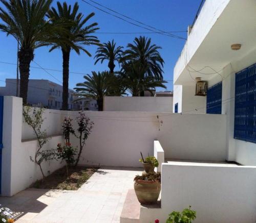 una casa blanca con palmeras y una valla en L'espadon de Mahdia Maison avec petit jardin en Mahdia