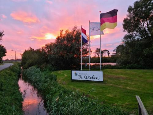 three flags on the side of a river with a sign at Chalet 531a op Recreatiepark De Wielen in Sint Maarten