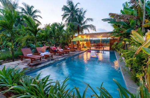uma piscina em um resort com cadeiras e palmeiras em New Sunshine Homestay em Hoi An