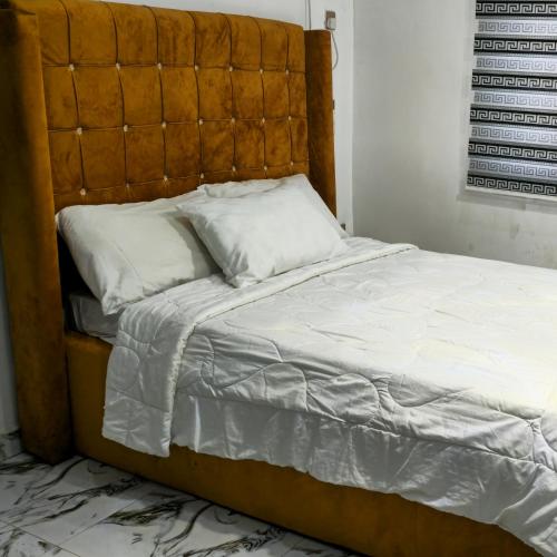 1 cama con cabecero de madera y almohadas blancas en S&A Lump Apartments, Enugu, Nigeria, en Enugu