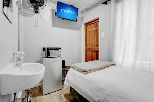 uma casa de banho com um lavatório, uma cama e uma televisão em The Bosau Guest House em Pretoria