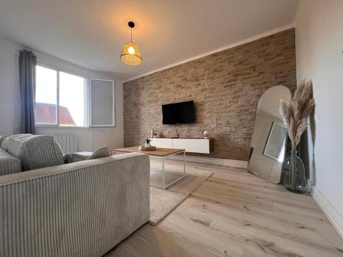 een woonkamer met een bank en een tv aan een bakstenen muur bij Logement chaleureux et lumineux in Villefranche-sur-Saône