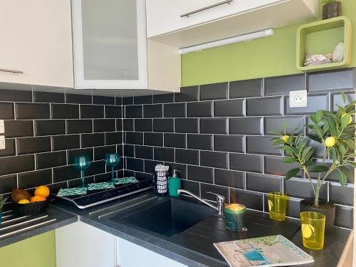 eine Küche mit einem Waschbecken und einer schwarz gefliesten Wand in der Unterkunft Studio Blue Horizon vue mer in Guidel-Plage