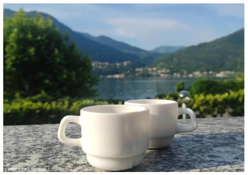 two white coffee mugs sitting on a table with a view at LFSUITE LuganoLake Terrazza Spiaggia privata Parking WI-FI Netflix in Porlezza