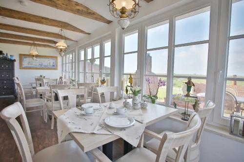 un comedor con mesas y sillas blancas y ventanas en Anker's Hörn - Hotel & Restaurant auf der Hallig Langeness en Langeneß