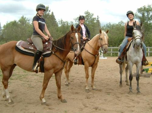 three women are riding on horses in the dirt at Meadowlark Cabin #5 in Maynooth