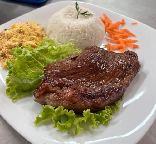 um prato de alimentos com carne, arroz e produtos hortícolas em Cassino Motel 4 em Santo André