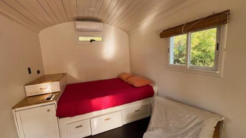 Un pequeño dormitorio con una cama roja y una ventana en La Casa Del Vagon, en Mar del Plata
