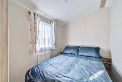a bedroom with a bed with blue sheets and a window at Water Sky Getaways 3-bedroom caravans at Durdle Door in Wareham