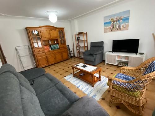 ein Wohnzimmer mit einem Sofa, Stühlen und einem TV in der Unterkunft Vivienda de Uso turístico Paseo del Suaron Vegadeo in Vegadeo