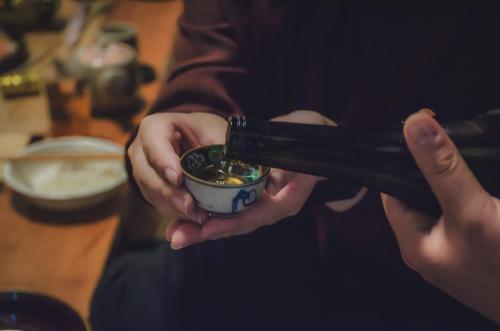 a person holding a chopstick in a bowl of food at 佐渡島 築120年の古民家一棟貸切 河崎浪漫館 囲炉裏体験 檜風呂-蔵サウナ完備 in Sado