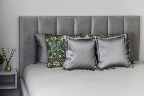 1 cama con cabecero gris y 4 almohadas en Frida Elite Apartments en Šiauliai