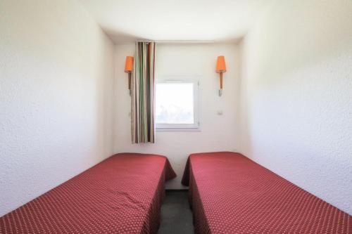 Cette petite chambre dispose de 2 lits rouges et d'une fenêtre. dans l'établissement Résidence Les Horizons d'Huez - maeva Home - Appartement 2 Pièces 5 Personnes - Confort MAE-2570, à Huez