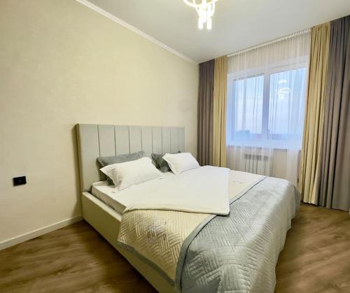um quarto com uma cama grande e uma janela grande em Апартаменты в ЖК "AURUS" em Almaty