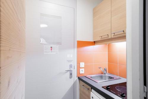 une petite cuisine avec un évier et une porte. dans l'établissement Résidence Plagne Lauze - maeva Home - Studio 2 Personnes - Confort MAE-0154, à Mâcot La Plagne