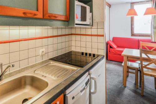 une cuisine avec un évier et un canapé rouge dans l'établissement Résidence Les Chalets des Arolles - maeva Home - Studio 4 Personnes - Confort MAE-8704, à La Plagne Tarentaise