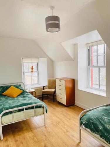 a bedroom with two beds and a dresser and two windows at The Crows Nest in Eyemouth