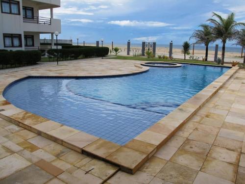 a swimming pool at the beach with palm trees and a building at Apartamento à beira-mar. Beachfront apartment in São Gonçalo do Amarante
