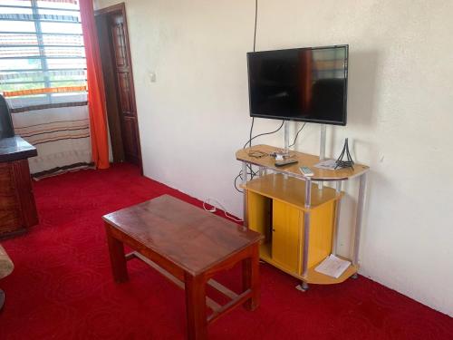 a living room with a tv and a table and a tv stand with a television at Hotel La Rochelle in Bonamakolo