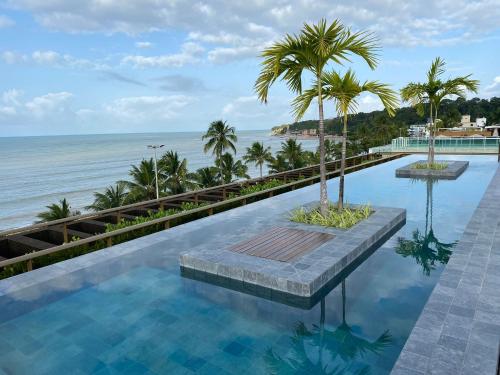 a swimming pool with palm trees and the ocean at Beautiful Accommodation - #Unity Flats Cabo Branco in João Pessoa