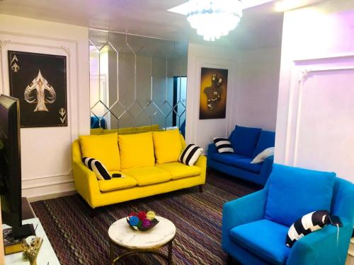uma sala de estar com um sofá amarelo e cadeiras azuis em willy-richy Apartments em Ikeja