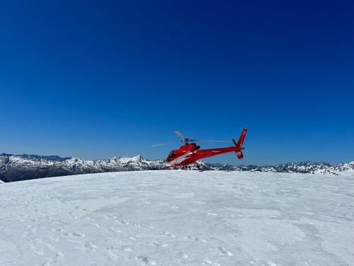 czerwony helikopter latający nad śniegiem pokrytą górą w obiekcie Drifting Sands Beachfront Retreat w mieście Hokitika