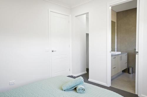 a white bedroom with a bed and a bathroom at The Robinson - Host on the Coast in Connewarre