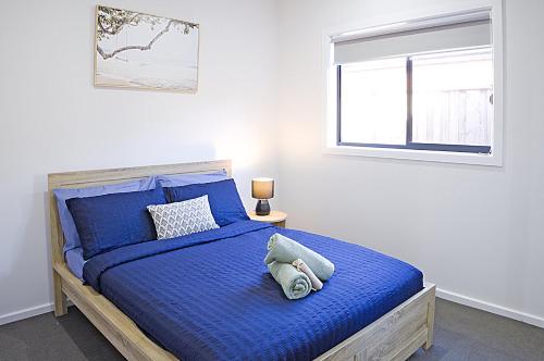 a bedroom with a blue bed with a window at The Robinson - Host on the Coast in Connewarre