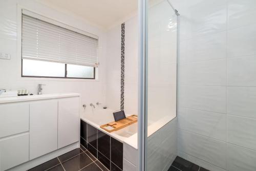 baño blanco con ducha y lavamanos en Spacious and Restful Holiday Home with Backyard en Weetangerra