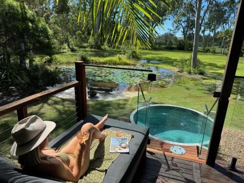 a woman laying on a couch next to a swimming pool at Lake Weyba Cottages Noosa in Peregian Beach