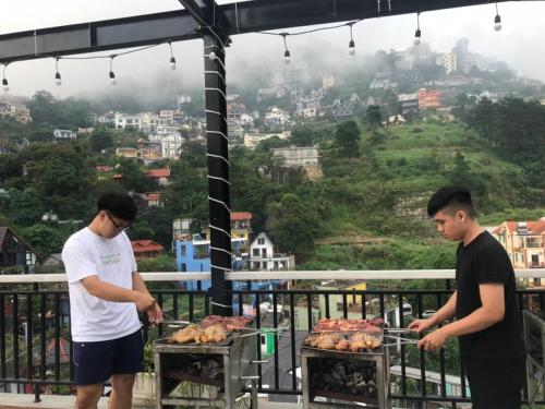 Dois homens estão a cozinhar galinhas num grelhador numa varanda. em Hương Trà Villa - Hotel Tam Đảo em Tam Dao