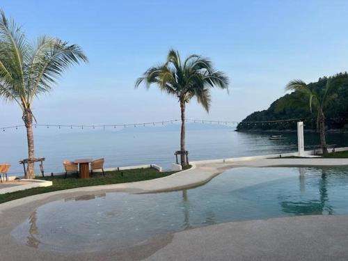 a swimming pool next to the ocean with palm trees at Le Shelby Samui Beach Resort Cottage in Koh Samui 