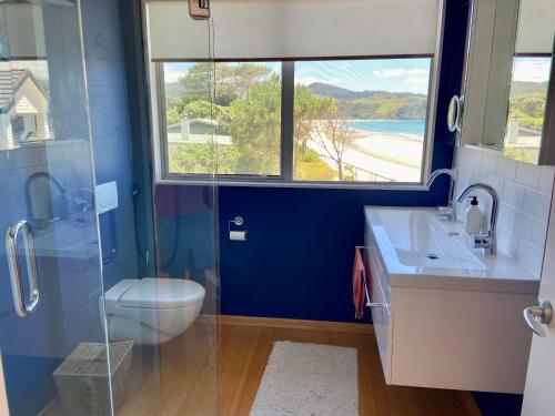 a bathroom with a toilet and a sink and a window at Bliss on the Beach - Whangapoua in Whangapoua