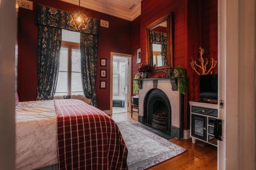 Lake Daylesford Country House في ديلسفورد: غرفة نوم بجدران حمراء وسرير ومدفأة