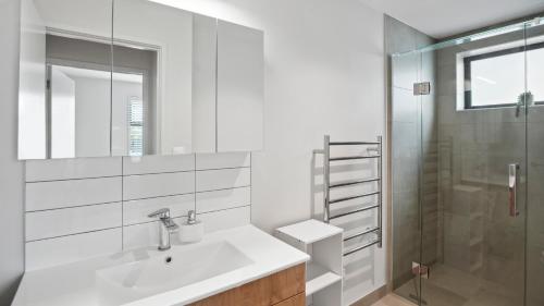 a white bathroom with a sink and a shower at Residence De La Mer - Orewa Holiday Home in Orewa