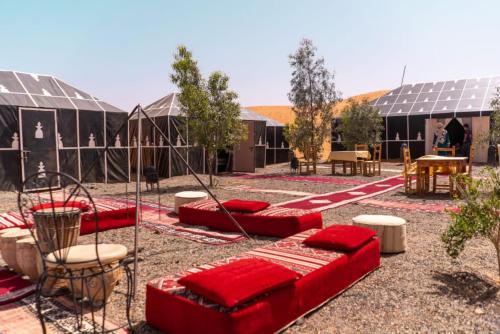 a courtyard with red cushioned chairs and tables and buildings at Holiday Desert Camp in Merzouga