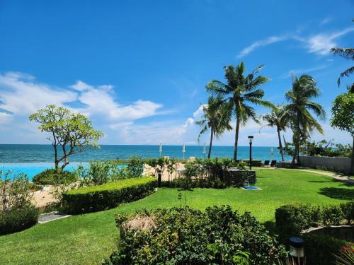 a garden with palm trees and the ocean in the background at Baan Ploen Talay (บ้าน เพลินทะเล ชะอำ) in Cha Am