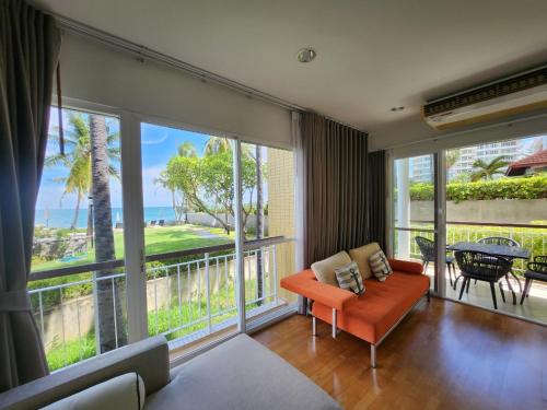 a living room with an orange couch and large windows at Baan Ploen Talay (บ้าน เพลินทะเล ชะอำ) in Cha Am