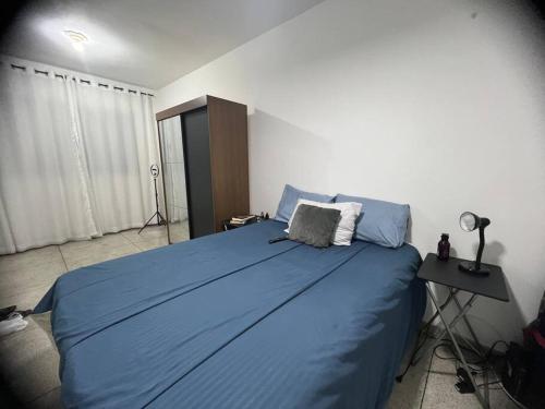een slaapkamer met een bed met blauwe lakens en een bureau bij Kitnet beira-mar em São Vicente in São Vicente