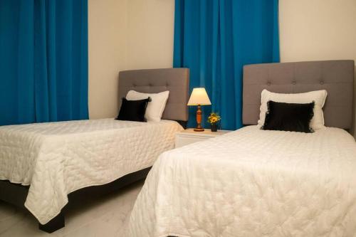 two beds in a room with blue curtains at Cozy Beach House in La Romana