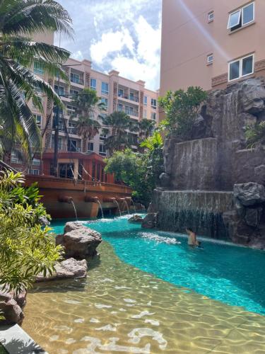 a pool in a resort with a waterfall and a person in the water at Atlantis Condominium Resort Pattaya in Jomtien Beach