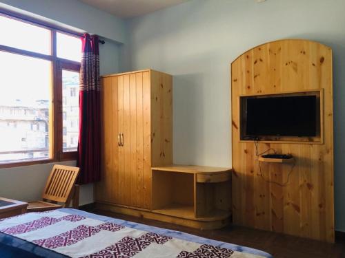 HOTEL CORNER RETREAT BnB في مانالي: غرفة نوم مع تلفزيون وخزانة خشبية