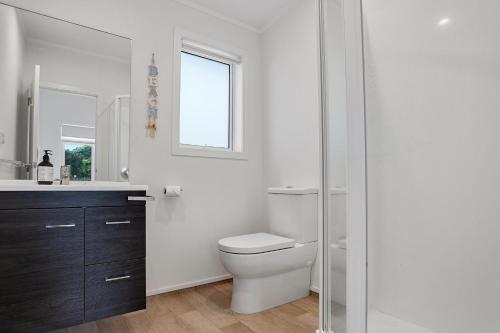 een badkamer met een toilet, een wastafel en een raam bij Modern Kiwi Bach - Waihi Beach Holiday Home in Waihi Beach