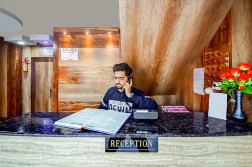 un hombre sentado en un escritorio hablando por celular en OYO Hotel Ambika Dx, en Gwalior