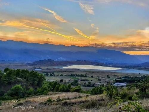 a sunset over a field with a lake and mountains at Mateo & Sara Guesthouse. in Libohovë