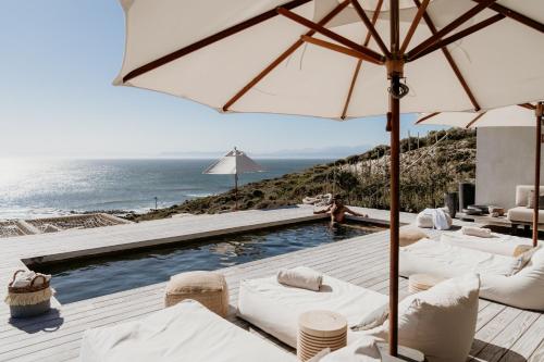 a pool with white chairs and an umbrella and the ocean at Pure Sea Boutique Lodge in Gansbaai