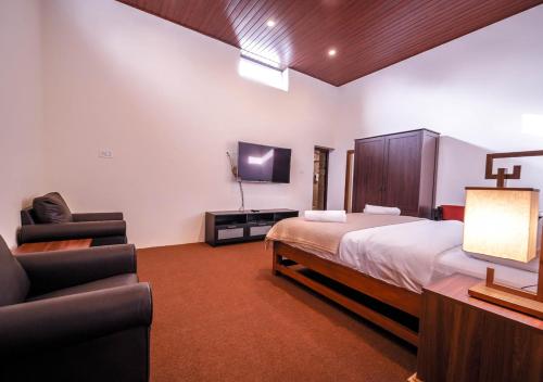 um quarto com uma cama, uma televisão e cadeiras em Lauriston Villa Ooty by VOYE HOMES em Ooty