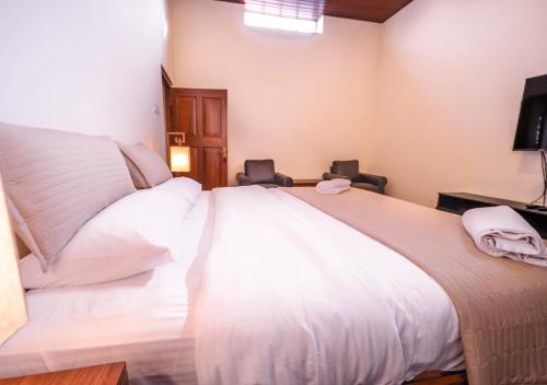 a bedroom with a large white bed with two chairs at Lauriston Ooty Town Heritage Bungalow by VOYE HOMES in Ooty