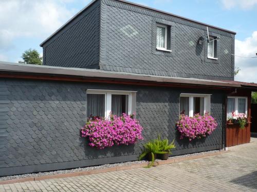 une maison noire avec des fleurs roses dans des boîtes de fenêtre dans l'établissement Holiday Home in Neustadt am Rennsteig with Pond, à Neustadt am Rennsteig